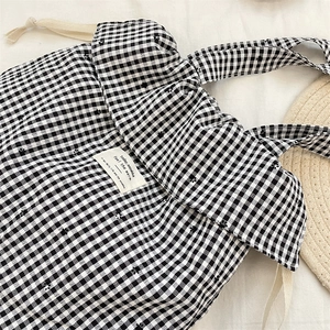 Close-up of black and white gingham tote bag with floral embroidery and white woven label