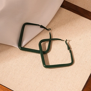 Macro detail of glossy dark green square geometric earrings on soft beige fabric
