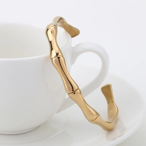 Vue détaillée du bracelet jonc doré style bambou à côté d'une tasse à café blanche