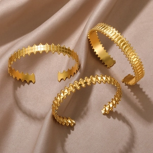 Detailed view of three gold-plated textured cuff bracelets on a champagne silk fabric background