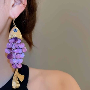 Detail of fish-shaped earrings with purple shell scales and gold metal fringe on model