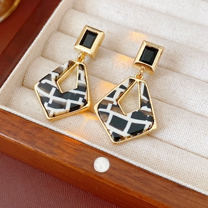 Macro shot of gold square earrings with black and white resin on a soft velvet display