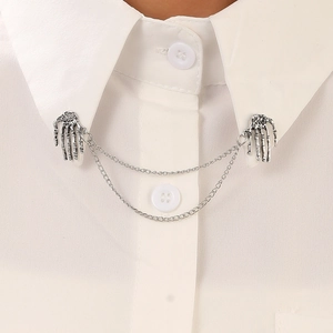 Close-up of gothic silver skeleton hand collar pin with double chains on white shirt