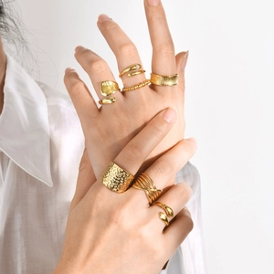 Close-up of stacked gold stainless steel rings with hammered and smooth textures on a model
