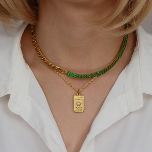 Close-up of layered gold necklaces with emerald green zircon and sun tarot pendant