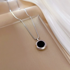 Detail of silver box chain with black circular pendant on white silk and golden tray