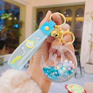 Detail of moon-shaped acrylic keychain with blue silicone strap and golden bell charm