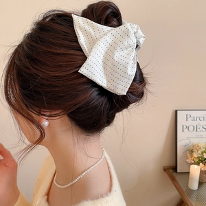 Detailed view of a white fabric bow hair clip with blue polka dots on an elegant updo hairstyle