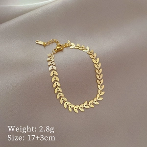 Detailed view of golden leaf-shaped stainless steel bracelet on champagne satin fabric