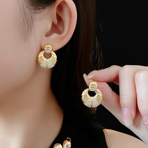 Détail de boucles d'oreilles dorées en forme de coquille avec zircons sur l'oreille