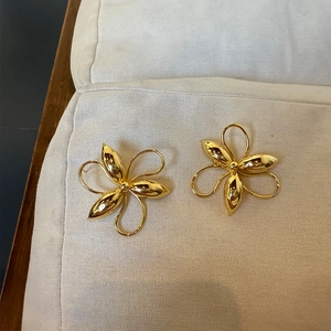 Detailed view of large gold floral earrings with a metallic texture on soft white padding