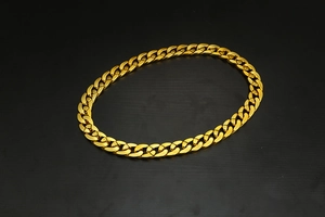 Close-up of a chunky golden hip hop style Cuban link necklace on a dark wood background