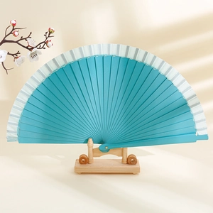 Minimalist solid wood folding fan in teal green with elegant white fabric edges on a stand