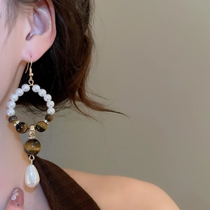 Detail of vintage tiger eye and pearl drop earring worn on a model with golden finish
