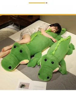 Détail de coussins crocodiles en peluche verte de deux tailles sur un lit douillet