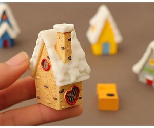 Close-up of a miniature Christmas snow house model held in fingers to show small scale