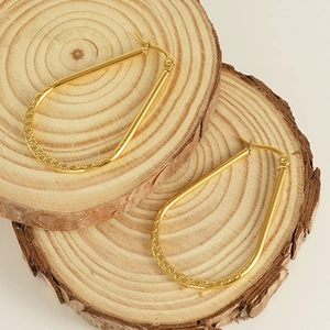 Detailed view of textured 18K gold plated oval earrings on natural wood blocks