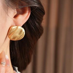 Detailed close-up of matte gold pleated geometric earring with wavy texture on model