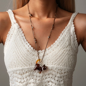 Detail view of brown resin cat pendant necklace with pearl bow and woven rope on model