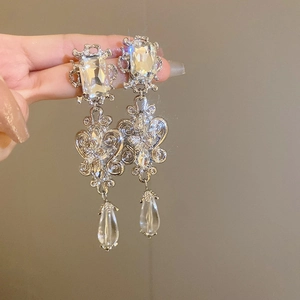 Detail of silver drop earrings featuring clear crystals and intricate hollow metal patterns