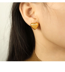 Gros plan d'une boucle d'oreille dorée en forme de cœur rayé portée par un mannequin