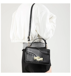 Detail of black crossbody bag with crocodile texture and golden wavy metal buckle