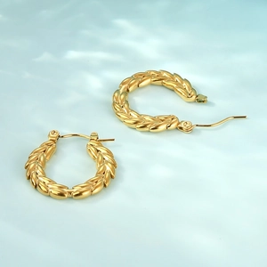 Detailansicht goldener Ohrringe mit Ährenmuster und polierter Edelstahl-Oberfläche