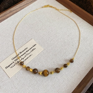 Detail of vintage beaded necklace with tiger eye stones on a wooden tray with a card