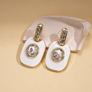 Détail de boucles d'oreilles dorées avec émail blanc et cristaux étincelants