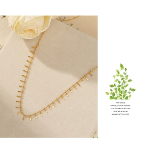 Detail of gold thin chain necklace with vertical bar pendants on a beige display stand