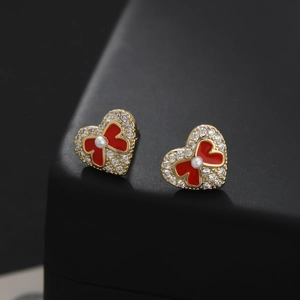 Elegant gold heart earrings with red enamel bow and pearls on black jewelry box