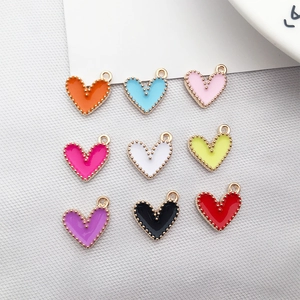 Flat lay of nine colorful heart-shaped alloy pendants on a white fabric background