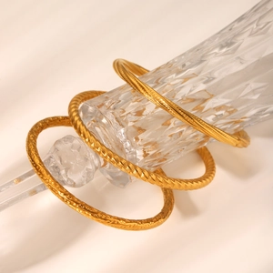 Close-up of three textured gold-plated stainless steel bangles on a glass bottle