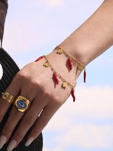 Close-up of gold stainless steel bracelets featuring red chili and four-leaf clover charms