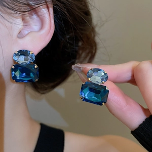 Detailed close-up of oval and rectangular blue crystals on gold-plated stud earrings