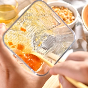 Hand holding a container with yellow silicone spatula mixing food in a kitchen setting