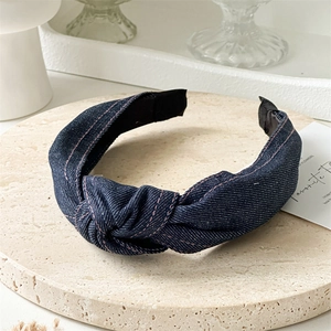 Détail d'un serre-tête en denim bleu foncé noué sur un plateau en pierre avec texture