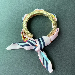 Detailed macro of a matte gold cuff bracelet wrapped with a pink floral silk scarf