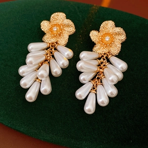Détail de boucles d'oreilles fleurs dorées avec zircons et pampilles de perles blanches