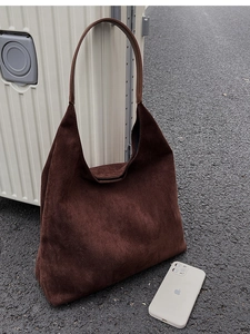 Close-up of deep coffee matte suede bucket bag next to a beige suitcase for size comparison