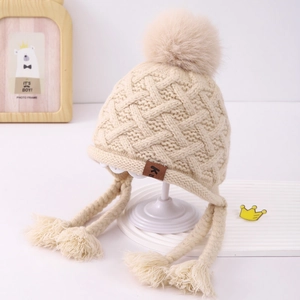Detail of beige knit baby hat with large faux fur pompom and braided ear flaps
