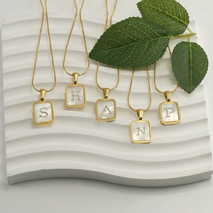 Gold plated titanium steel necklaces with lettered white shell square pendants on display