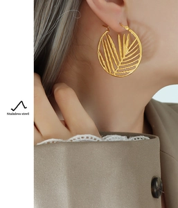 Detailed close-up of golden hollow palm leaf earrings in stainless steel on a model