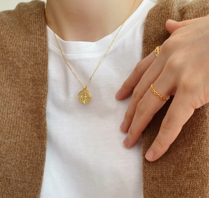 Detail of gold coin necklace and chain ring on model wearing cozy knit cardigan