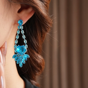 Close-up of elegant silver earrings with heart-shaped blue crystals on a model