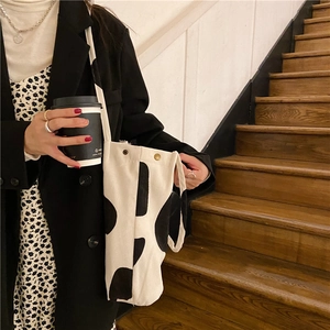 Detalle de un bolso tote grande de pana con estampado de vaca en blanco y negro y ojales metálicos