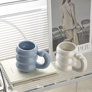 Detail of blue and pearly white ceramic mugs with bubbly texture on glass shelf