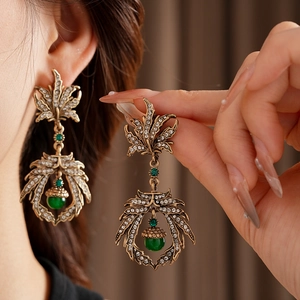 Detail of vintage gold leaf earrings featuring clear crystals and a green gemstone drop