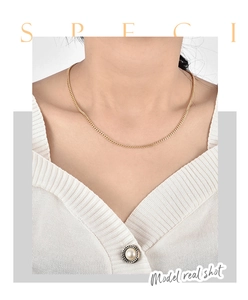 Close-up of minimalist gold plated Cuban link chain necklace on model wearing white cardigan