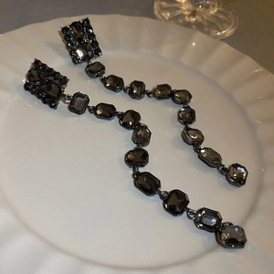 Detail of dark crystal tassels on square geometric earrings over white ceramic plate